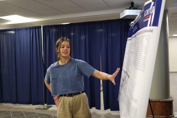 A student makes a presentation beside a poster at the 2024 学生 Conference for 研究, 专业活动, 及创意艺术